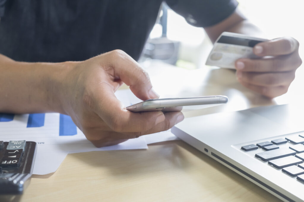 A man holding mobile phone and credit card on laptop for online